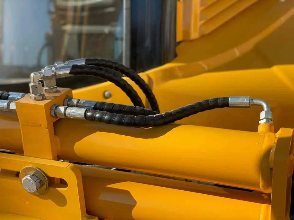 Hydraulic hoses and fittings on a yellow machine cylinder