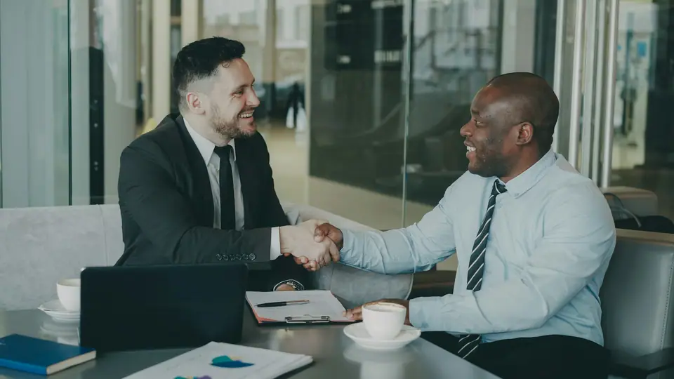 Two business people shaking hands across a meeting table